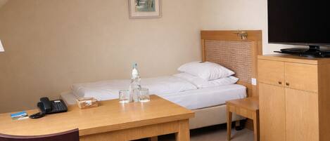 A hotel room with a bed, a desk with a phone, a television, and a chair.