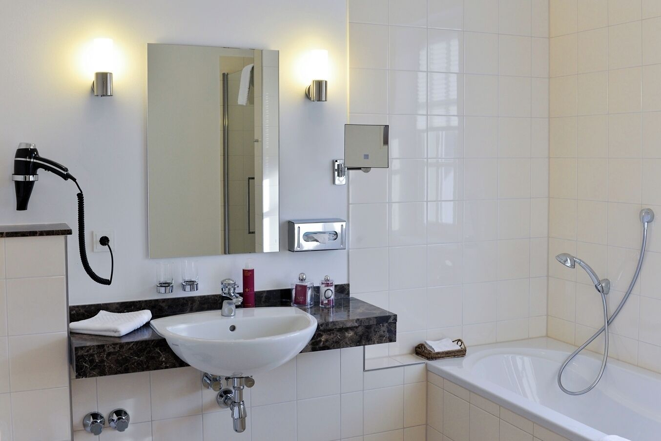 A modern bathroom with a white sink, a mirror, a hairdryer, a shower, and a bathtub.
