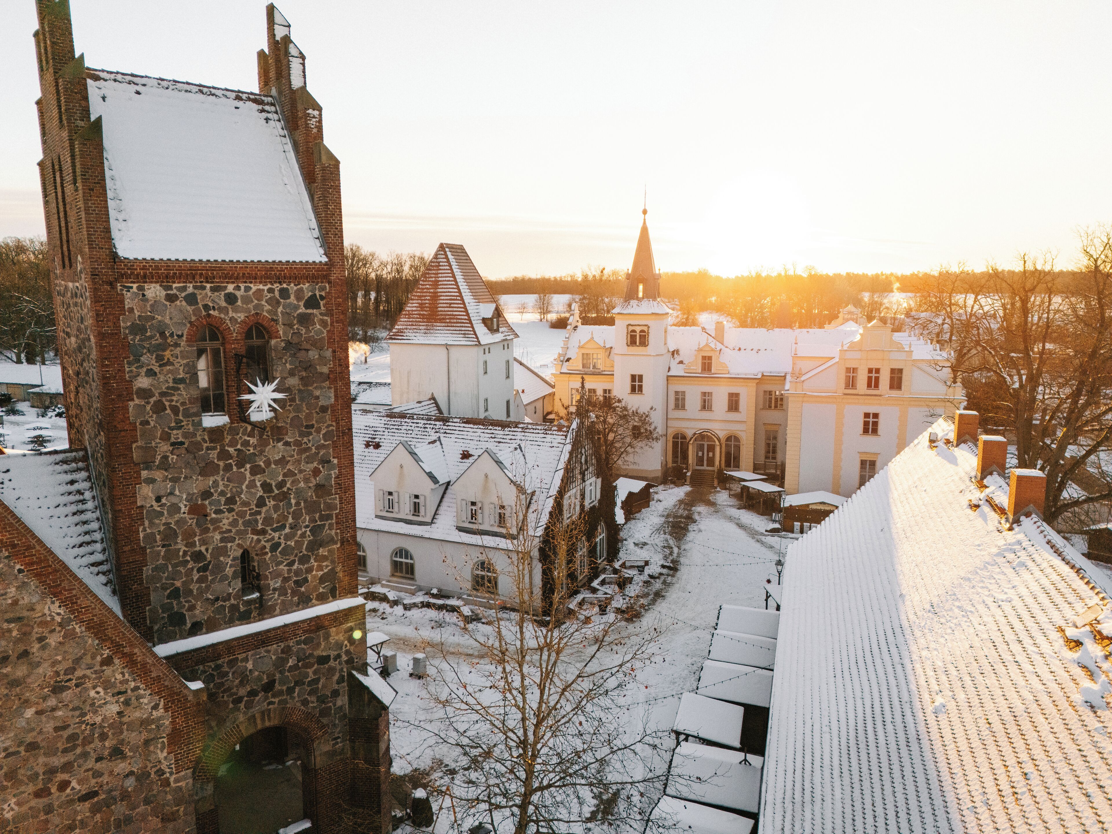 Een historisch complex van gebouwen, waaronder een toren en een kerk met een spits, gelegen in besneeuwde omgeving.