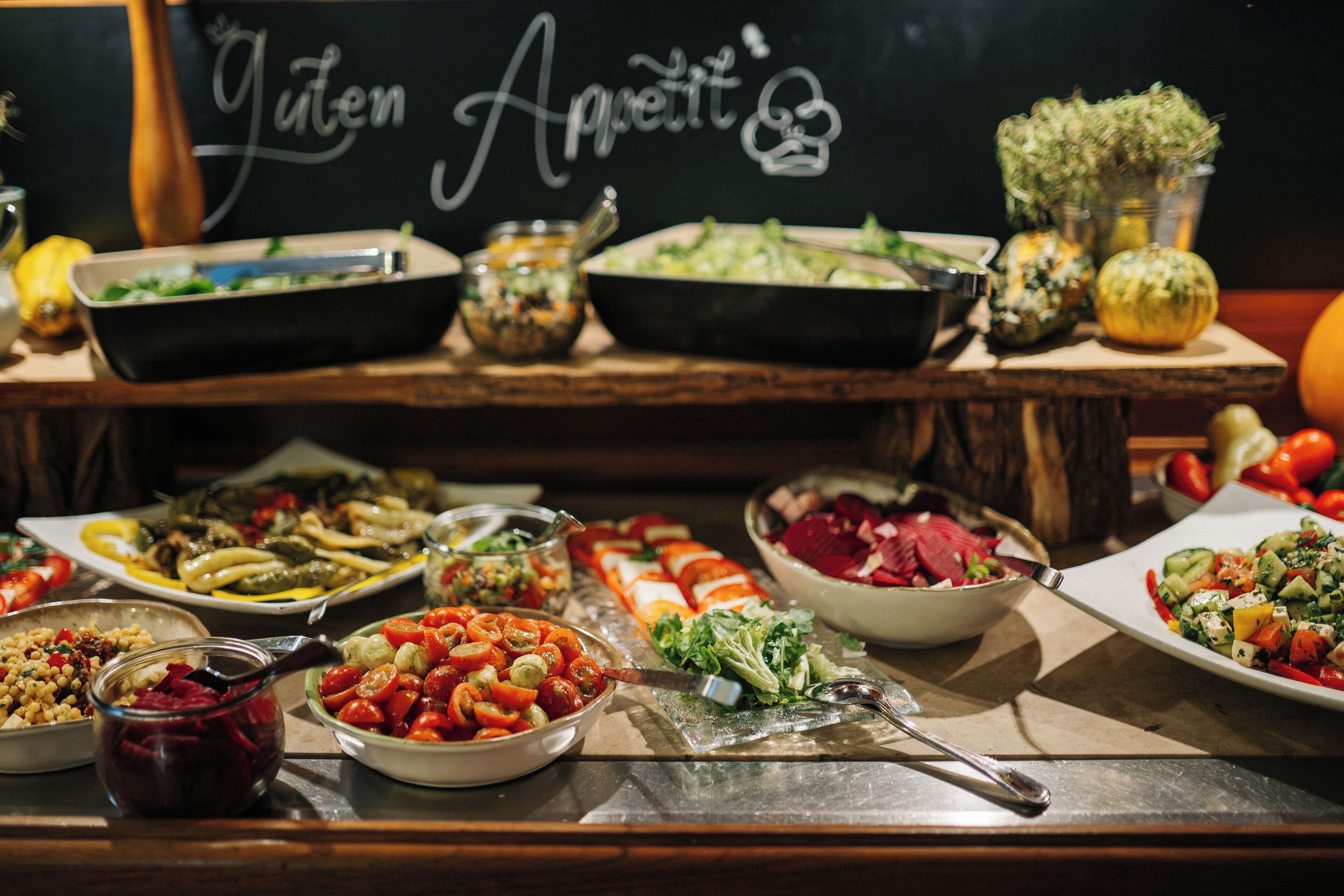 Une table de buffet proposant divers plats, et un panneau noir sur lequel est écrit : « Bon appétit ».