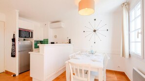 A kitchen with white cabinets, a microwave, and a refrigerator. There is a dining table with chairs and a pendant light above it. - Apartment in Dramont Near Beaches & Casino (Saint-Raphael)