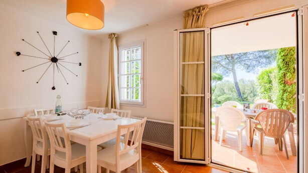 A dining area with a white table and chairs, a modern wall art piece, and a sliding glass door leading to an outdoor patio with additional seating. - Apartment in Dramont Near Beaches & Casino (Saint-Raphael)
