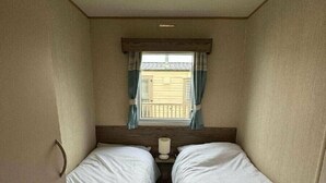 Ein kleines Hotelzimmer für Einzelpersonen mit zwei Betten, einem Fenster mit Vorhängen und einem kleinen Tisch mit einer Lampe.