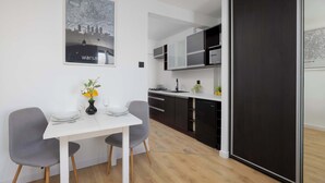 Una cucina moderna con mobili bianchi, un frigorifero nero e un'area pranzo con tavolo e due sedie bianche.