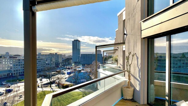 Eine moderne Wohnung mit Balkon und Blick auf eine Stadtlandschaft, einschließlich eines hohen Gebäudes und einer Kreisverkehrs.