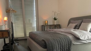 Ein Schlafzimmer mit Bett, Nachttisch, Lampe und einem Fenster mit Jalousien.