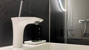 Ein modernes Badezimmer mit einer weißen Badewanne, einer schwarzen Shampooflasche und einer Duschkabine aus Glas.