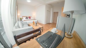 A hotel room with a bed, a sofa, a desk with a laptop, a lamp, and a view of the city. - Yankin Heights Hotel (Yangon)