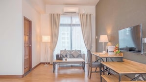 A modern hotel room with a wooden floor, a sofa, a dining table, a TV, and a window with curtains. - Yankin Heights Hotel (Yangon)