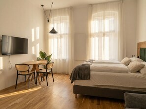 Quarto de hotel com uma cama, televisão, mesa de jantar com cadeiras e uma planta.