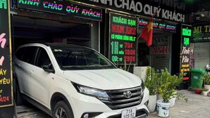 Ein weißer SUV parkt vor einem Gebäude mit Neonreklamen und einer roten Flagge.