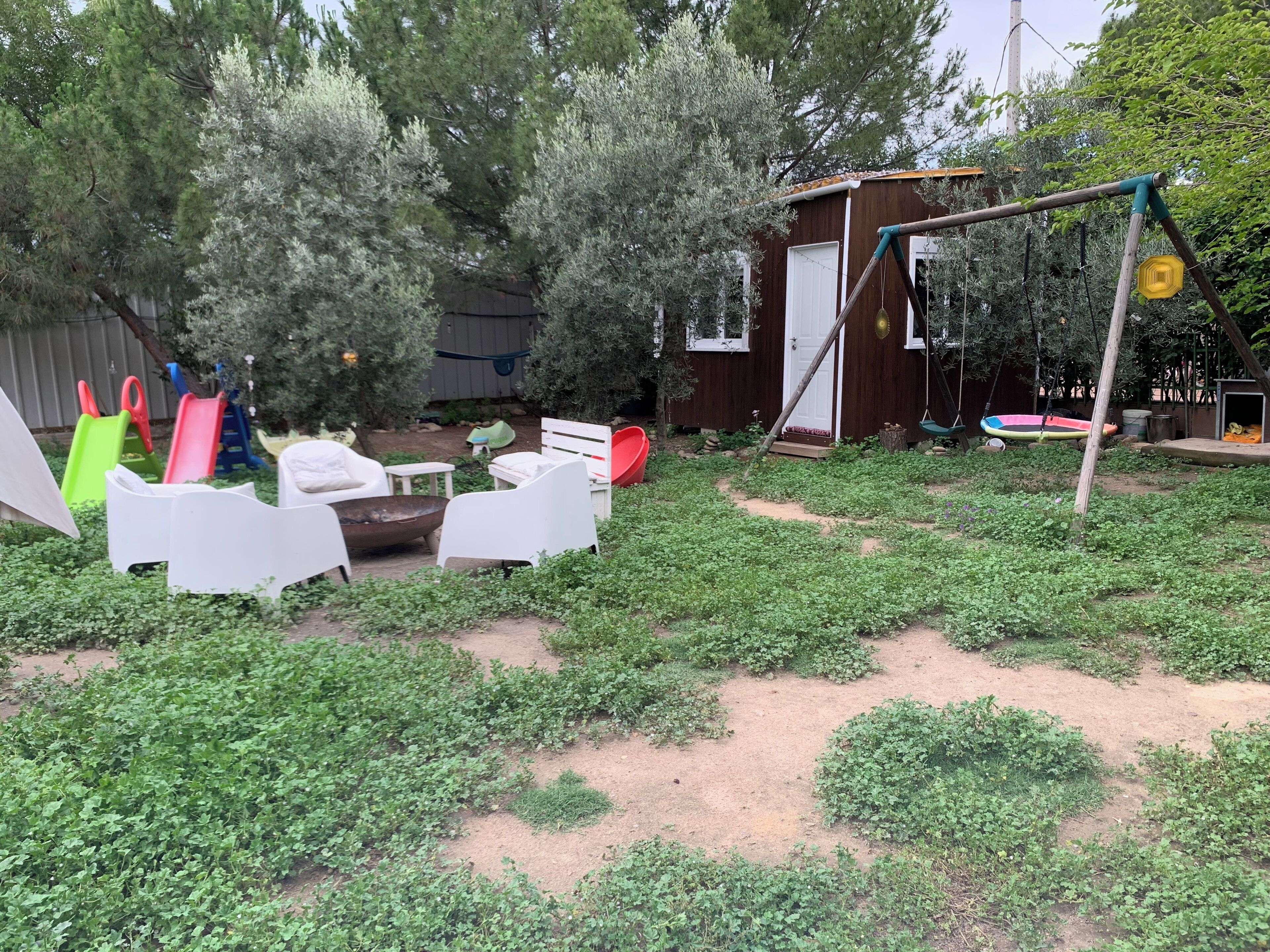 Un patio trasero con mobiliario exterior, un parque infantil y una pequeña construcción de madera.