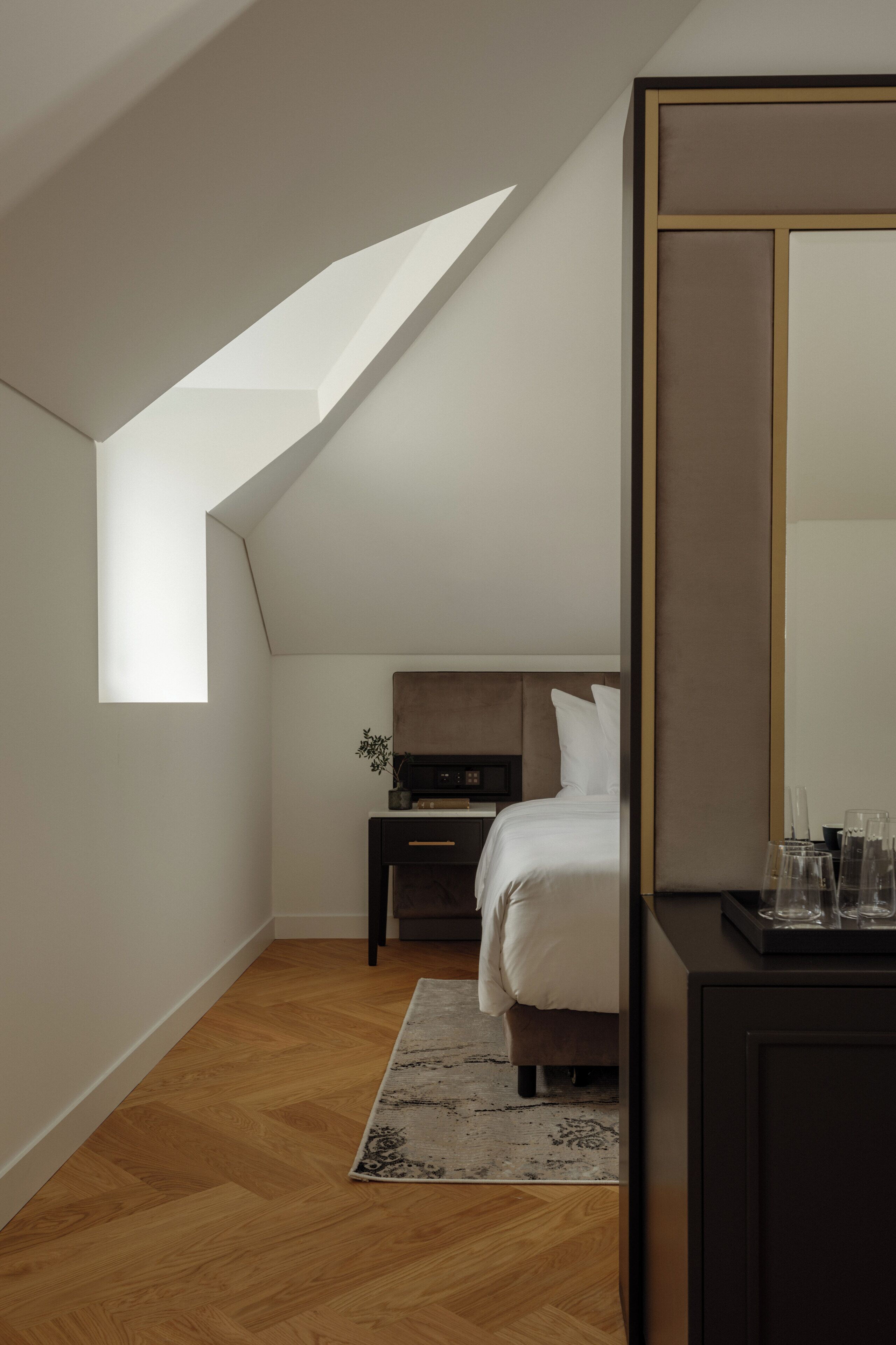 Ein Schlafzimmer mit schrägverdeckter Decke, einem Bett, einem Nachttisch, einer Kommode und einem großen Spiegel.