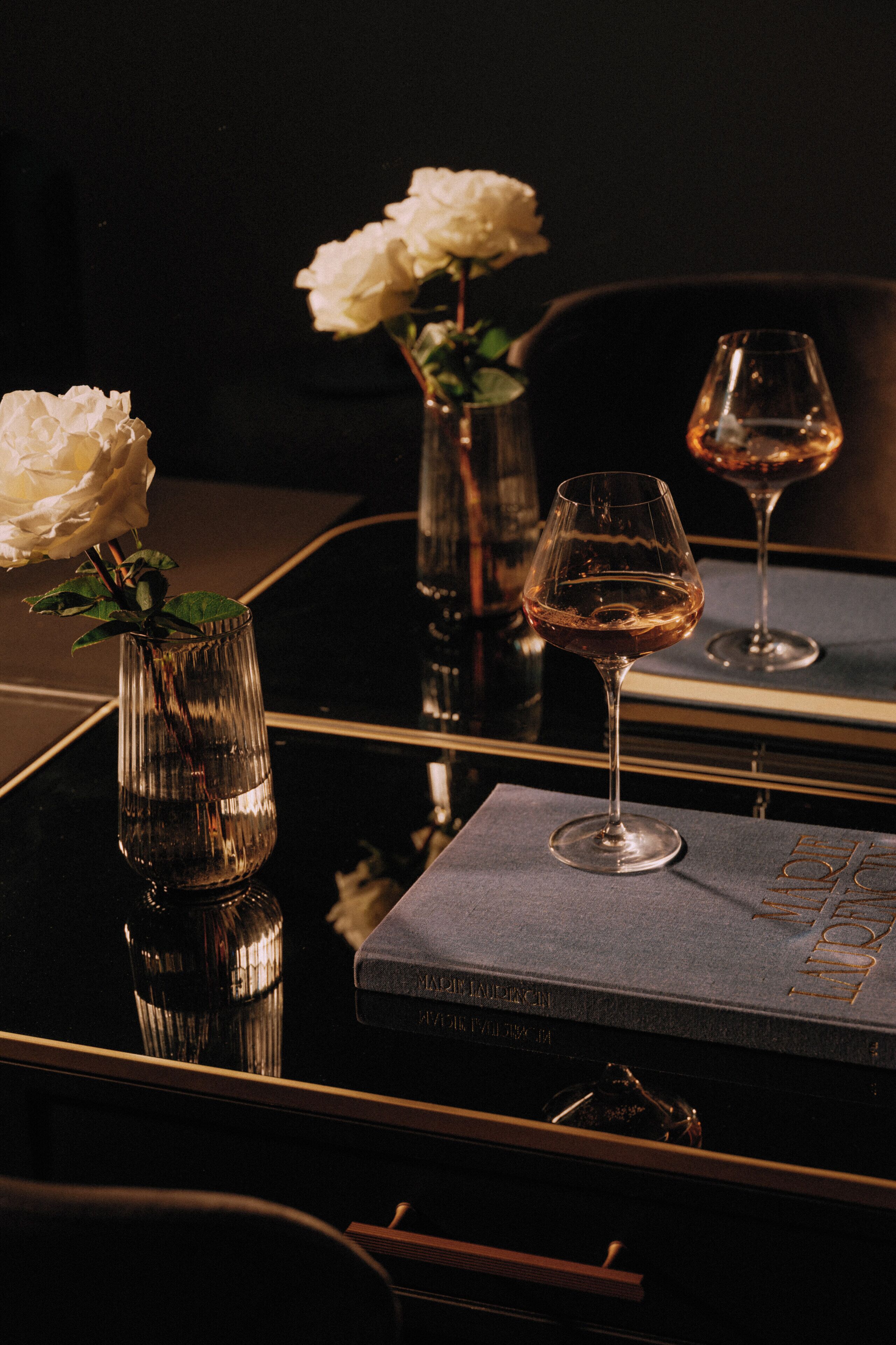Una mesa con un libro, dos jarrones con flores blancas y dos copas de vino.