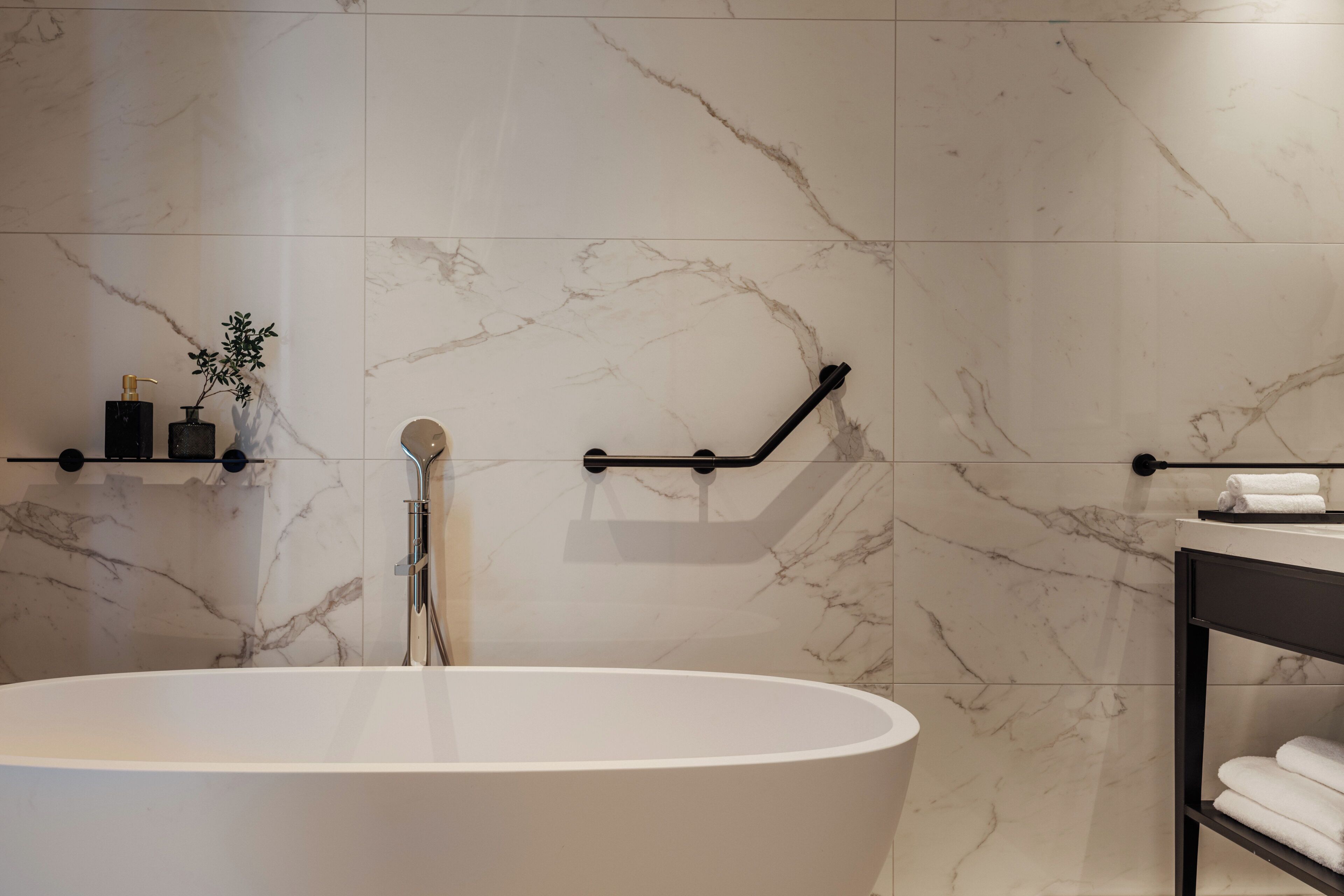 Un baño moderno con una bañera independiente, paredes de mármol y un perchero para toallas.