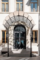 La entrada de un hotel con un dosel de hierro forjado, un letrero que dice 'HOTEL DE VOGUE N.Y.O.' y un conjunto de escalones de piedra que conducen a la puerta.