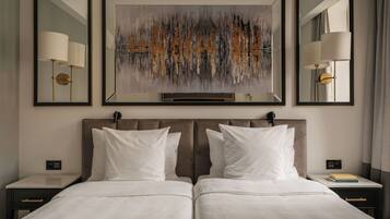 A hotel room with a large bed, two bedside tables, a nightstand, a wall-mounted artwork, and two floor lamps.