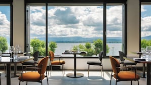 Comedor con una mesa dispuesta para cuatro, ventanas amplias con vista a un lago y montañas, y sillas con cojines.
