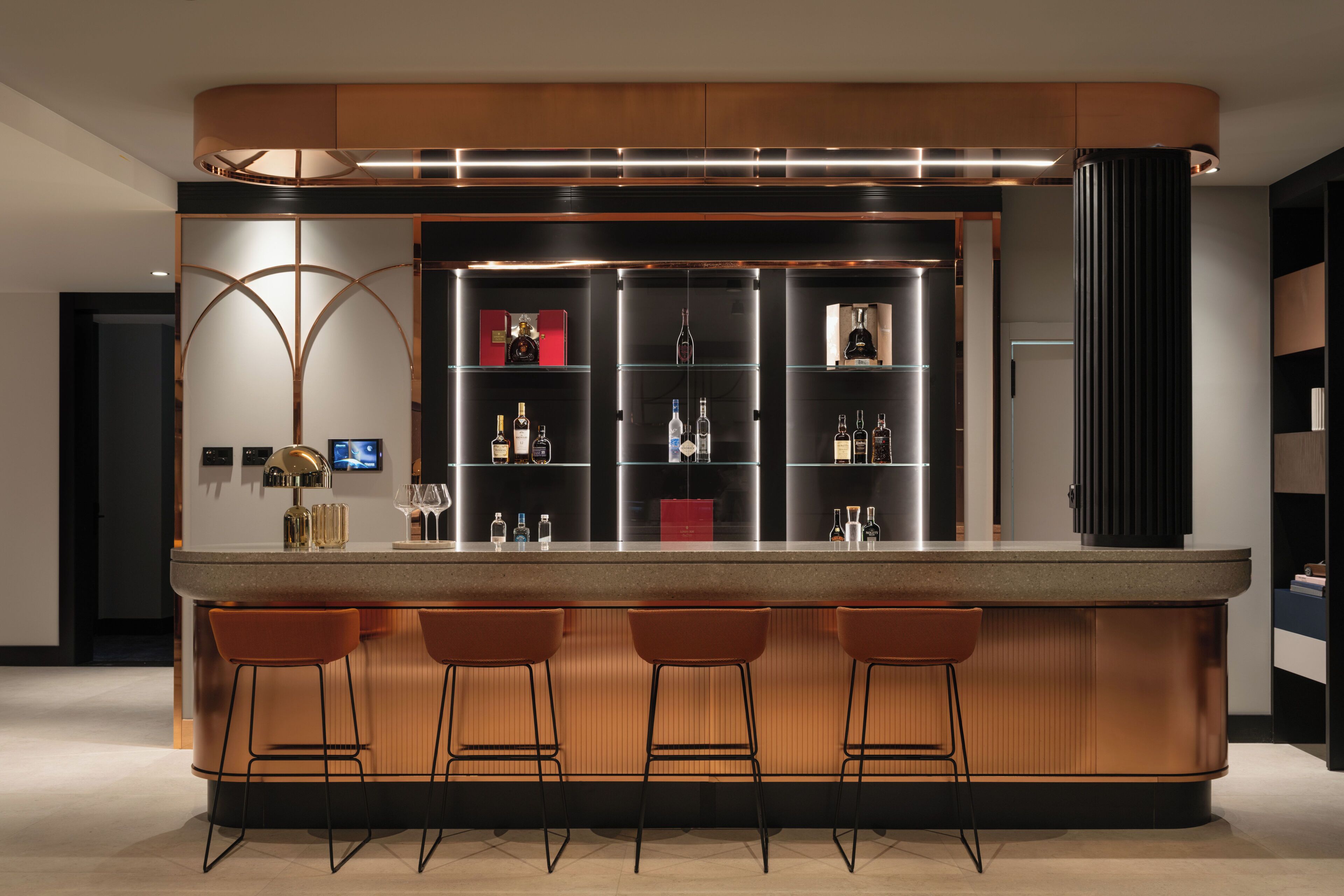 Zona de bar moderna con una barra curva, tres taburetes y una vitrina para vinos.
