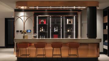 Zona de bar moderna con una barra curva, tres taburetes y una vitrina para vinos.