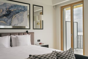 Habitación de hotel con una cama grande, una mesita de noche con lámpara, una obra de arte enmarco y vistas a través de una puerta corrediza.