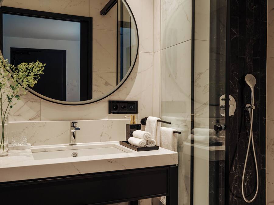 Een moderne badkamer met een marmeren wastafelmeubel, een grote spiegel, een douchecabine met glazen wanden en netjes opgevouwen handdoeken.