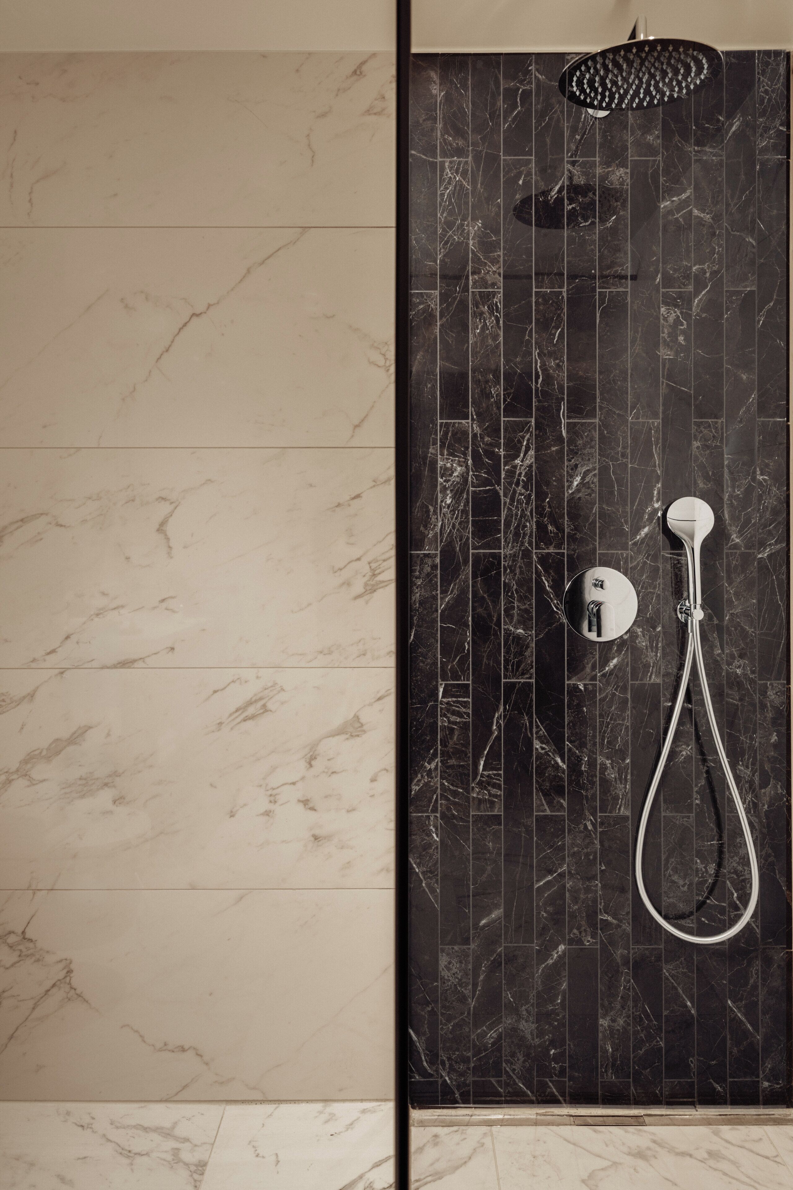 Une salle de bain avec une douche, un miroir et un mur orné d’un motif en marbre.