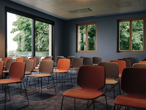 Un salón de conferencias con filas de sillas y mesas, ventanas amplias que dan a vistas de árboles e iluminación empotrada en el techo.