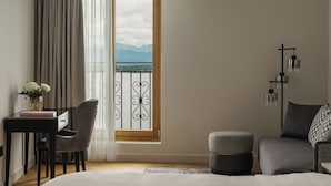 Habitación de hotel con cama, escritorio y silla, un pequeño otoman, mesita de noche y vistas a las montañas a través de una ventana.