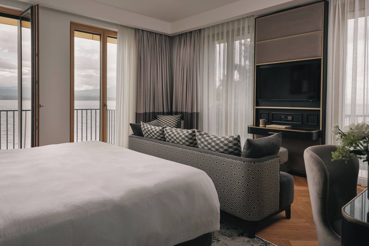 Moderni hotellihuone, jossa on suuri sänky, sohva, televisio ja näkymä merelle.