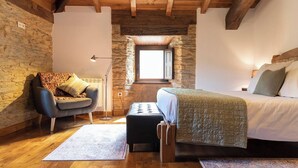 A cozy bedroom with a stone wall, wooden beams, a bed, a chair, and a small table. - Casa Liñeiras Solpor (A Pontenova)