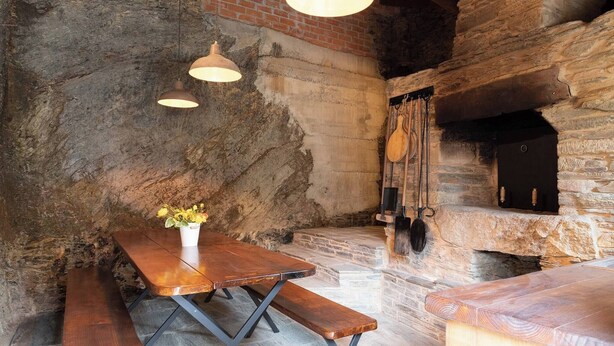 A rustic stone interior with a wooden table, benches, and a fireplace. - Casa Liñeiras Solpor (A Pontenova)