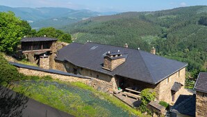 A stone building with a sloped roof, surrounded by lush greenery and hills. - Casa Liñeiras Solpor (A Pontenova)