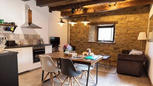 A modern kitchen with a wooden table, chairs, and a stone wall. - Casa Liñeiras Solpor (A Pontenova)