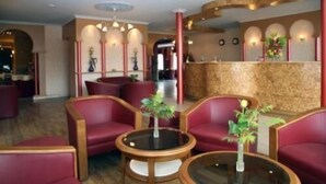 A lobby with red upholstered seating, round glass tables, and a reception area with a stone wall. - Hotel Eikenhof (Aalter)