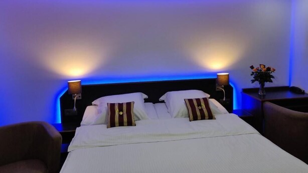 A hotel room with a neatly made bed, two bedside lamps, and a nightstand with a vase of flowers. - Hotel Eikenhof (Aalter)