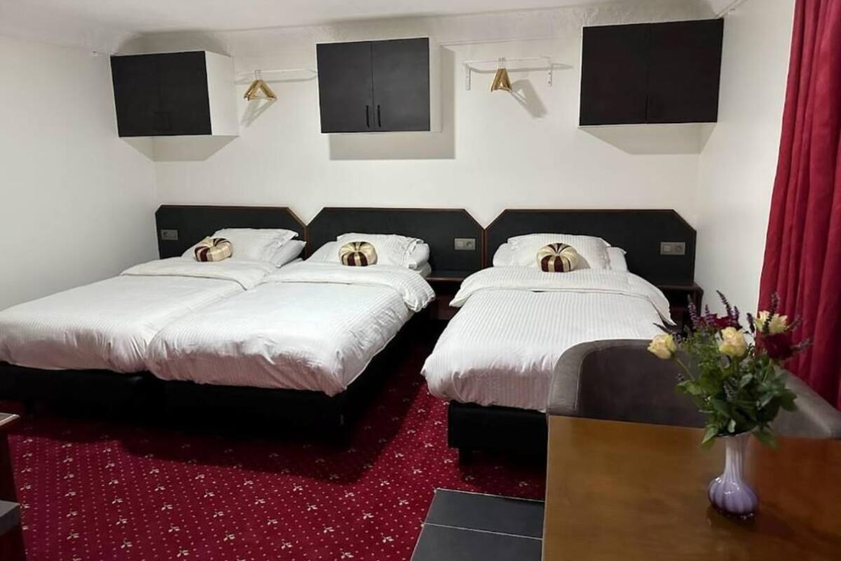 Ett hotellrum med två sängar, en röd matta, ett träbord och en vas med blommor.