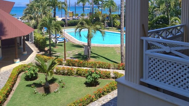 Vue sur un complexe hôtelier avec une piscine, des palmiers et un ciel bleu azur.