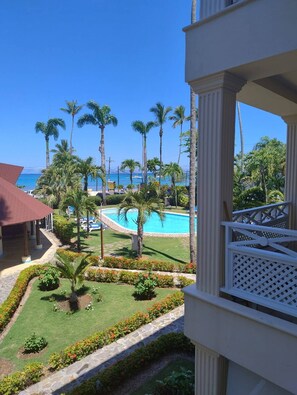 Vista de um resort com piscina, palmeiras e céu azul límpido.