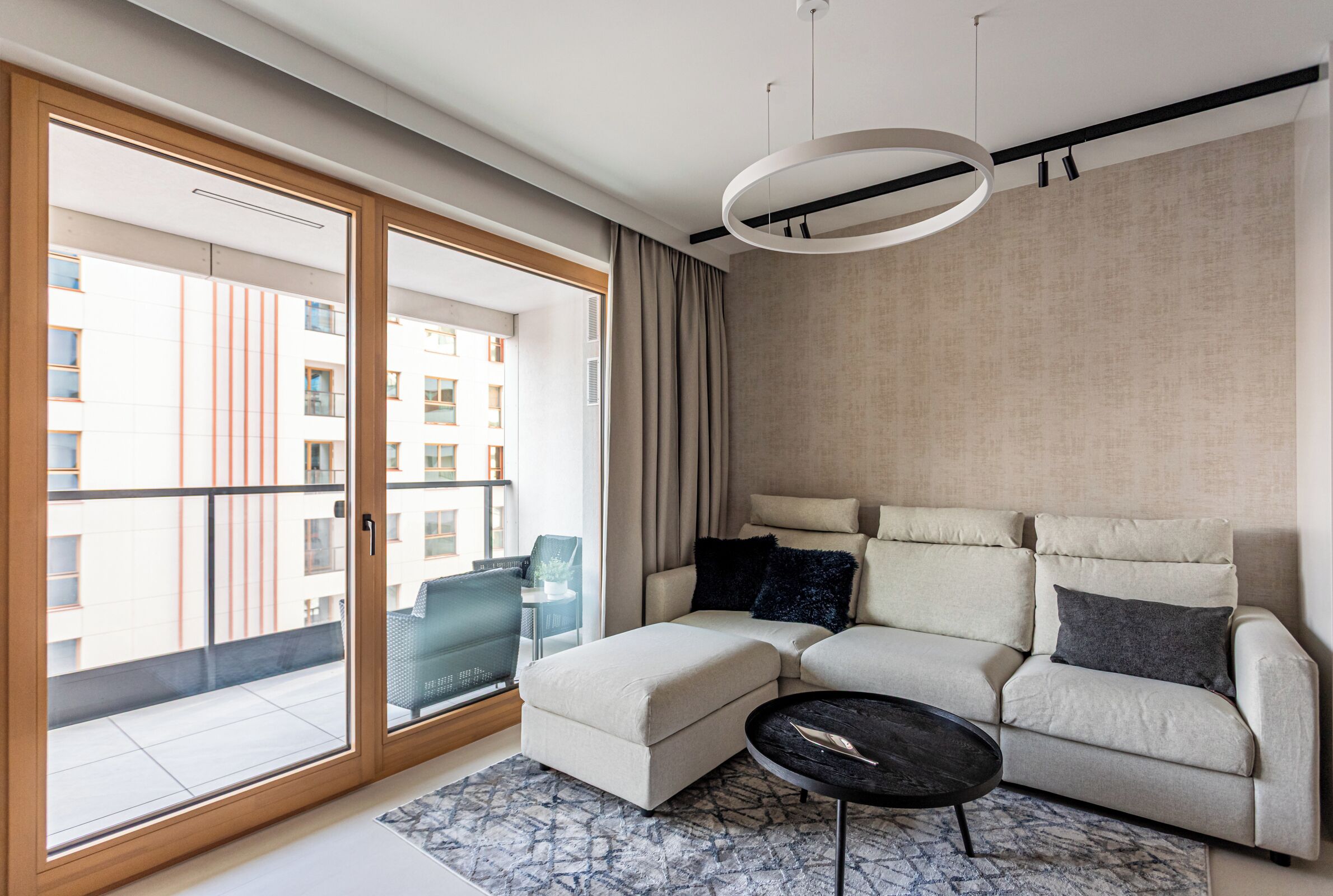 A modern living room with a sectional sofa, a round coffee table, and a large sliding glass door leading to a balcony.