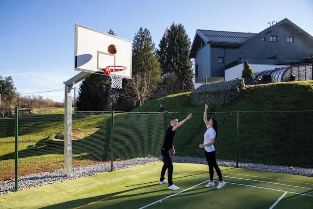An outdoor basketball court with a hoop, surrounded by a fence and a house in the background.