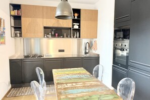 Moderni keittiö, jossa on puiset kaapit, ruostumattomasta teräksestä valmistetut kodinkoneet ja ruokapöytä tuoleineen.