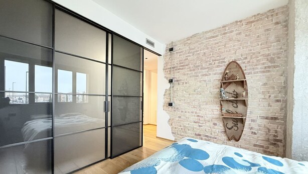 Un dormitorio con cama, puerta corrediza de vidrio, pared de ladrillo y repisas con adornos.