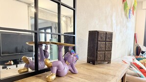Una habitación con un ventanal grande, una mesa de madera, una figurita de elefante púrpura y un armario de madera oscura.