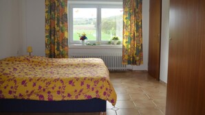 A bedroom with a bed, curtains, a window with a view, and a radiator. - Ferienwohnung im Obergeschoss, Homberg (Homberg)