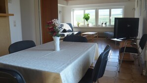 A dining area with a table set for four, a sofa, and a television in the background. - Ferienwohnung im Obergeschoss, Homberg (Homberg)