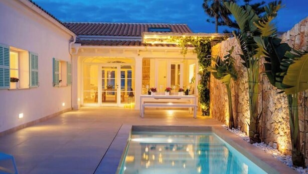A pool area with a bench, a stone wall, and a building with a tiled roof. - Veles Dos – Seafront Villa with Private Pool and Stunning Views (Sa Marina - Barcarés - Manresa)