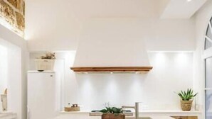 A modern kitchen with a central island, white cabinetry, and a stone accent wall. - Veles Dos – Seafront Villa with Private Pool and Stunning Views (Sa Marina - Barcarés - Manresa)
