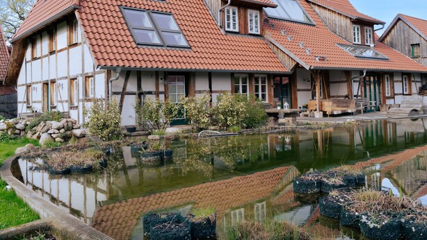 A traditional half-timbered house with a tiled roof and a pond in the foreground. - Remark Studios: Historic and modern Apartment (Burgwedel)