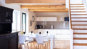 A modern kitchen with white cabinets, a wooden staircase, and a dining area with white chairs and a table. - Remark Studios: Historic and modern Apartment (Burgwedel)